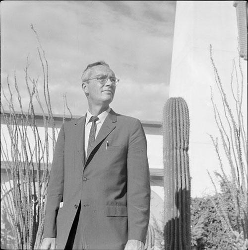 Poet Alan Dugan poses with cactus and ocotillo in the background outside the St. Thomas More Catholic Newman Center at the University of Arizona. This photo was taken during Dugan's visit for the Poetry Center's Fall 1966 Reading and Lecture Series. 